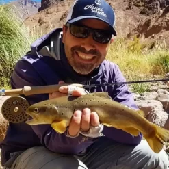 Pescador com mosca segurando uma truta marrom capturada em Mendoza – Pesca com mosca nos Andes.