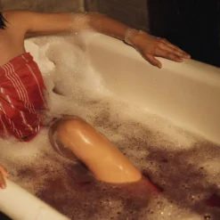 Person relaxing in a foamy bath wearing a red towel at a hammam spa