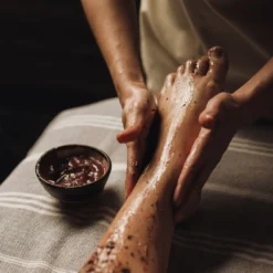 Spa therapist applying a body scrub treatment to a client's feet and legs
