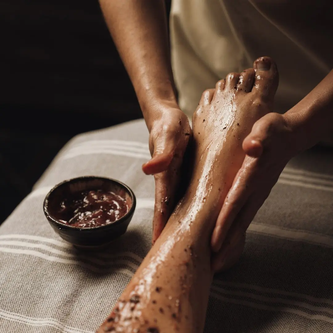 Spa therapist applying a body scrub treatment to a client's feet and legs