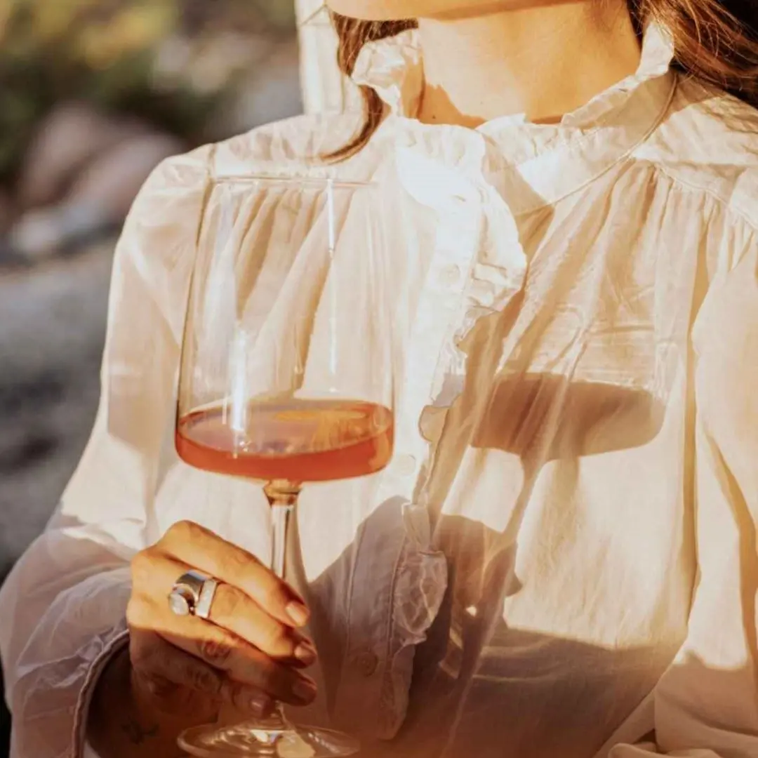 Woman in white blouse holding a glass of rosé wine in natural sunlight