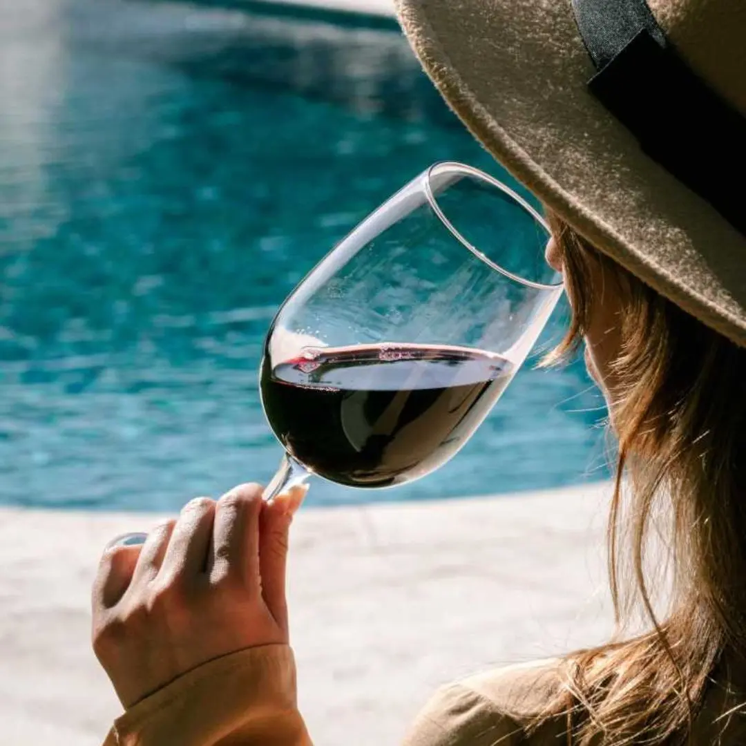 Woman in hat tasting red wine by a vineyard pool in Mendoza