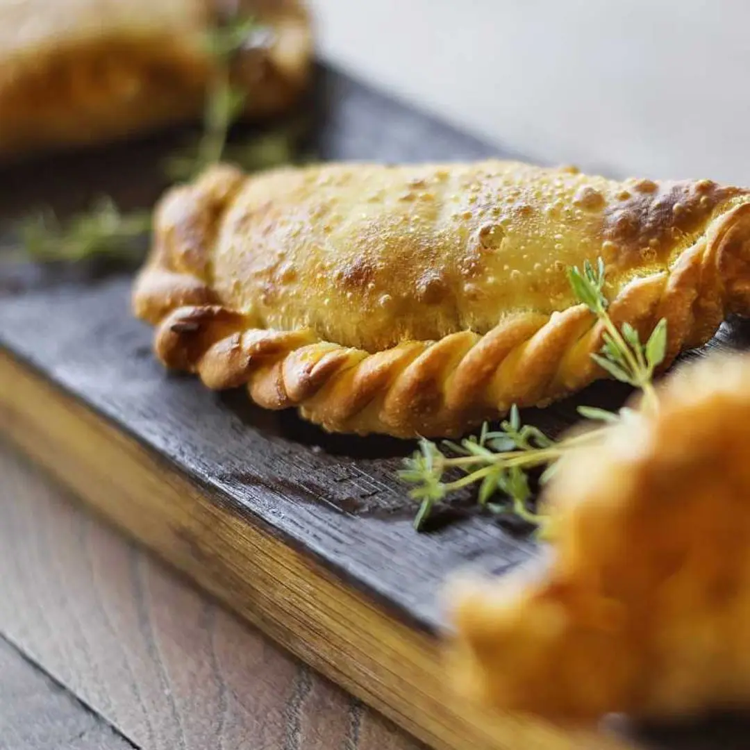 Golden baked empanadas on a wooden board with fresh herbs
