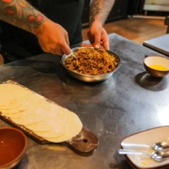 Mãos preparando recheio de empanada durante uma aula de culinária